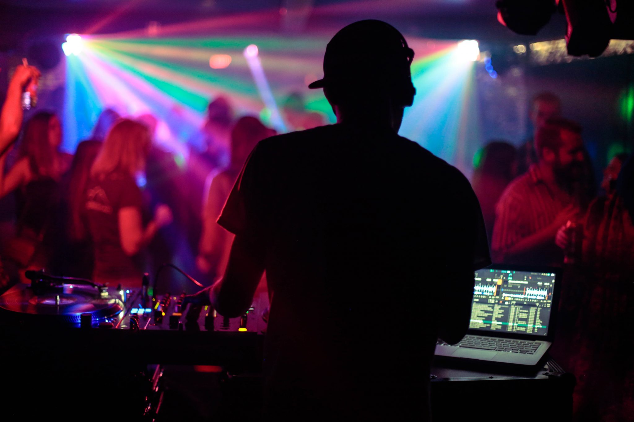 DJ and people dancing at party with colorful strobe lights