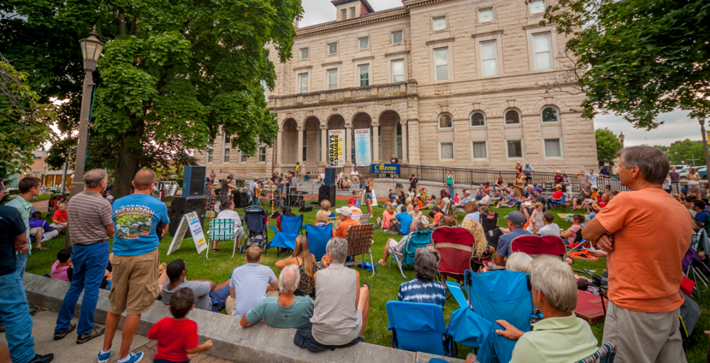 Large crowd of people sitting on lawn listening to speech