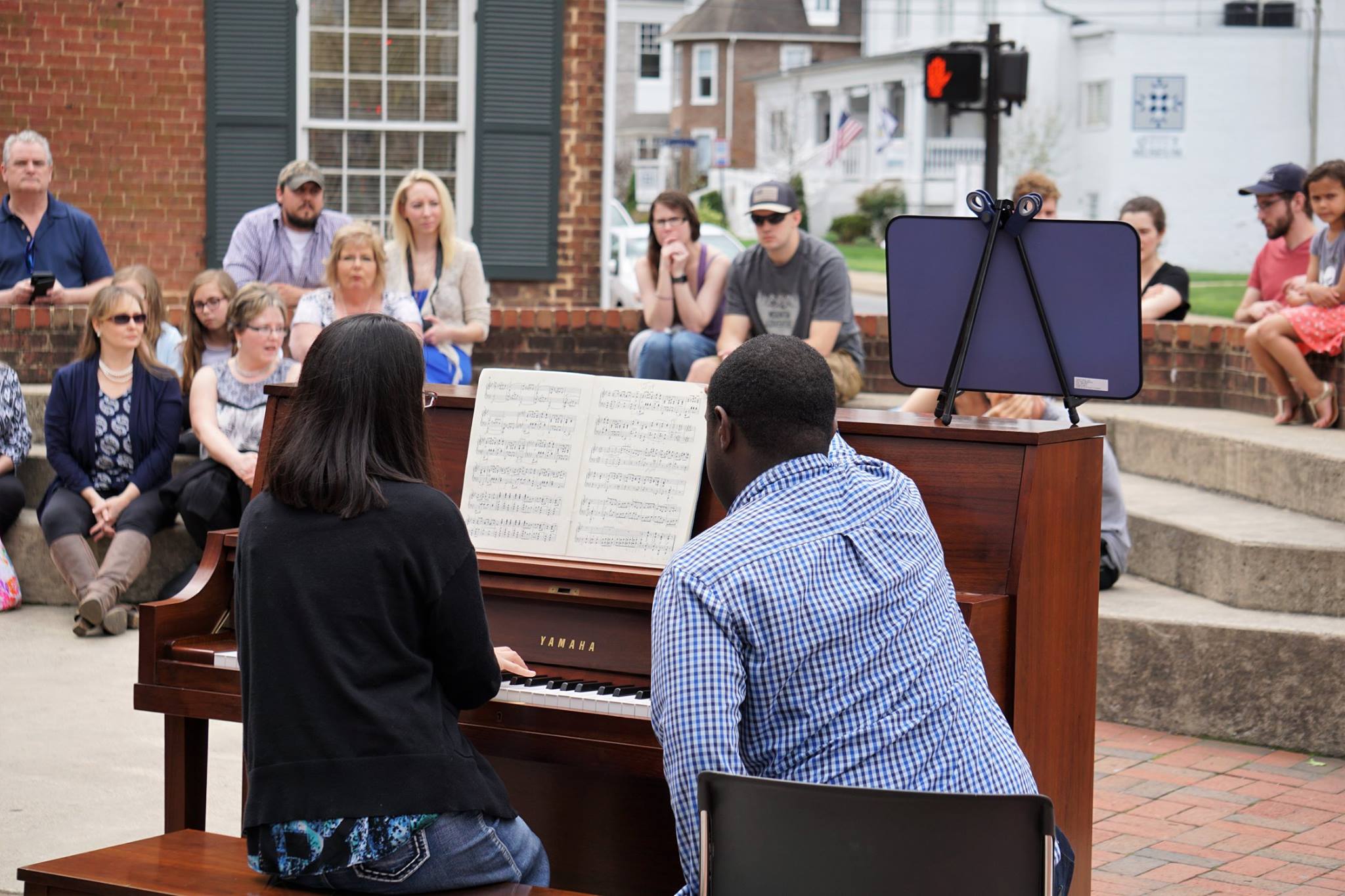 Woman playing piano with man turning pages and audience watching