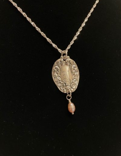 Gold necklace that is engraved with designs and a bead dangling at the bottom