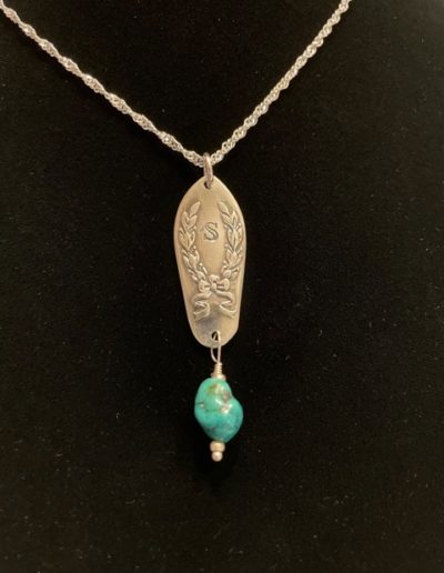 Gold necklace that is engraved with designs and a blue bead dangling at the bottom