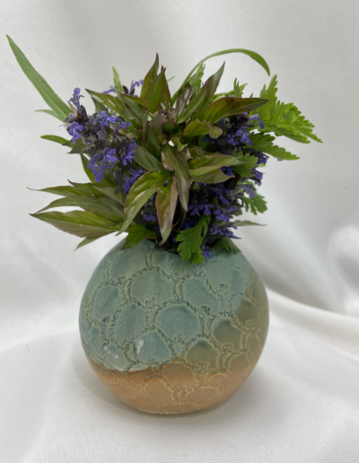 Blue and tan vase with purple flowers and green leaves