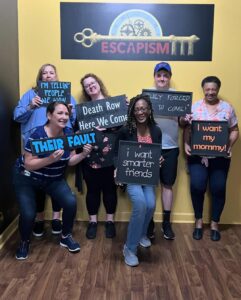 A group of people posing with signs outside of an escape room. 