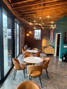 Inside of Rootstock Wine & Provisions. Dining tables with yellow chairs, teal walls, and unique light fixtures.